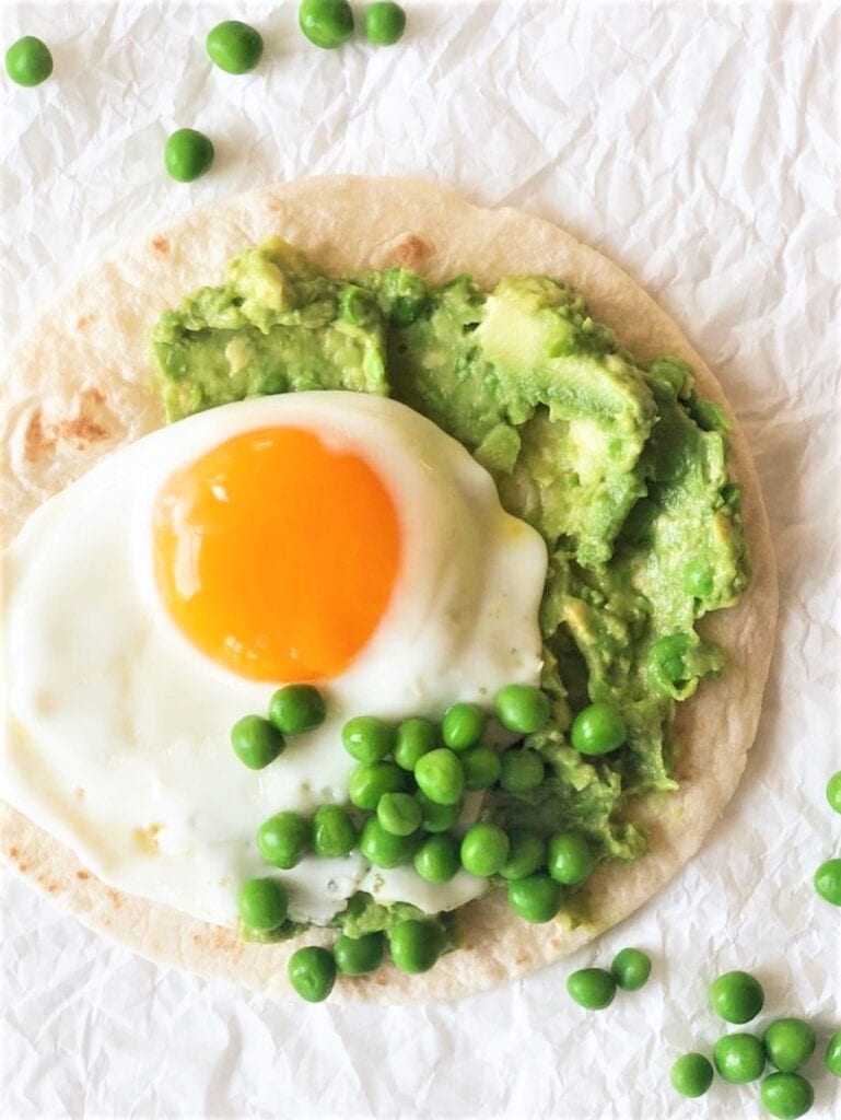 Overhead close up of a tostada with pea guacamole, fried egg and garnished with fresh peas.