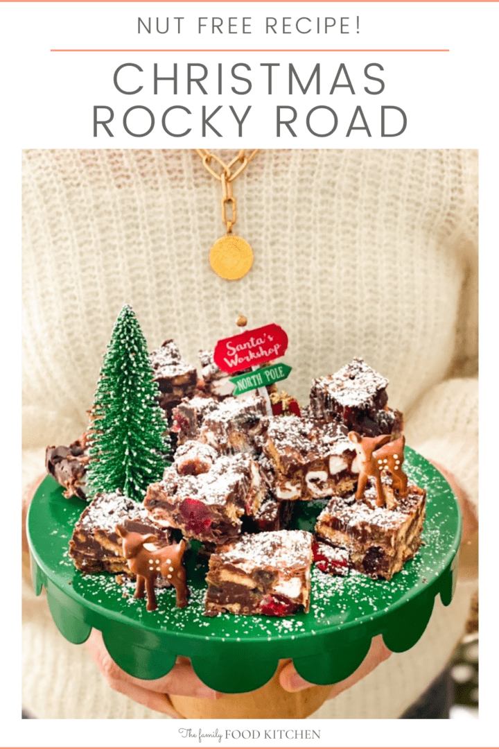 Pinnable image with recipe title and chocolate rocky road bars piled onto a green plate decorated with small artificial Christmas tree, toy reindeer and a small sign for the North Pole.