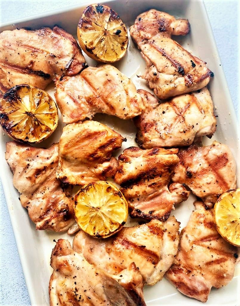 Roasting dish with grilled chicken thighs and lemon.