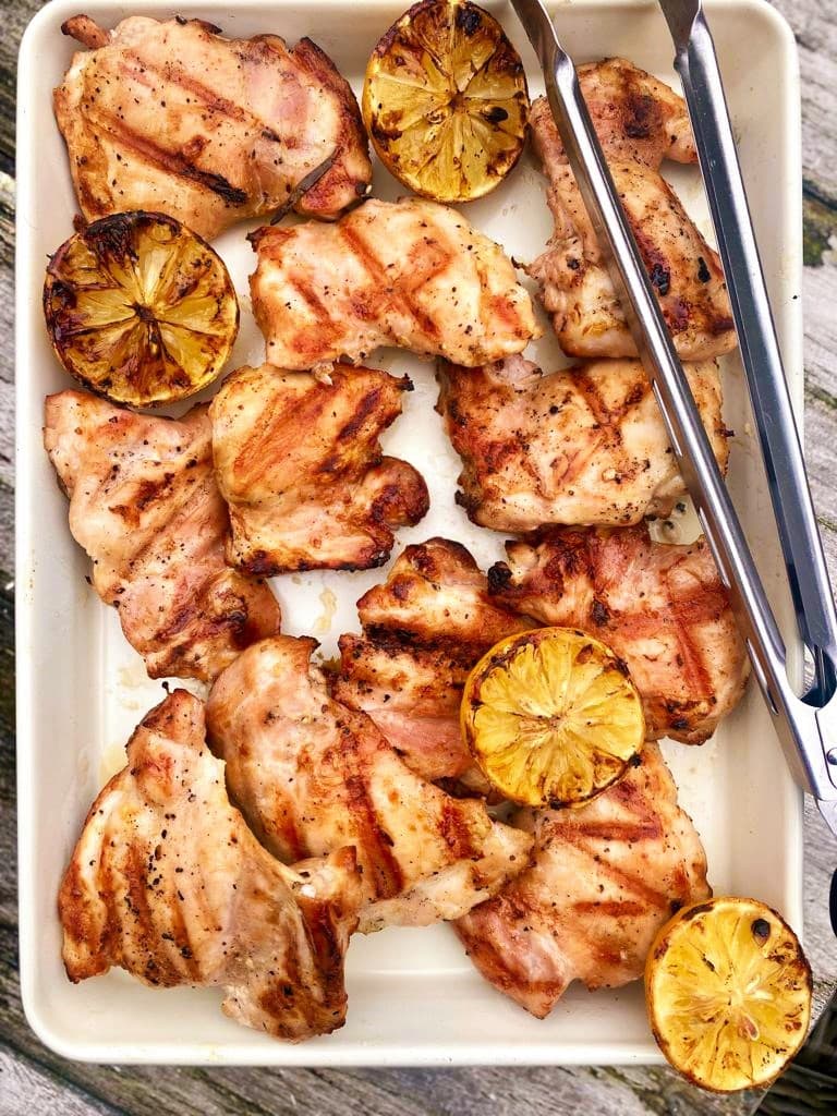 Roasting dish with grilled chicken thighs and lemon.