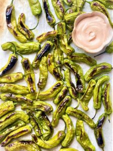 A tray with charred and blistered shishito peppers and a bowl of dipping sauce.