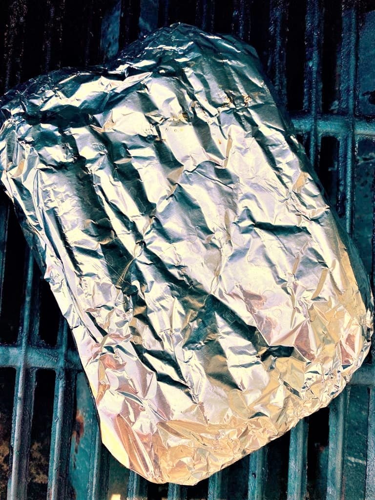A folded silver foil parcel set onto a BBQ grill.