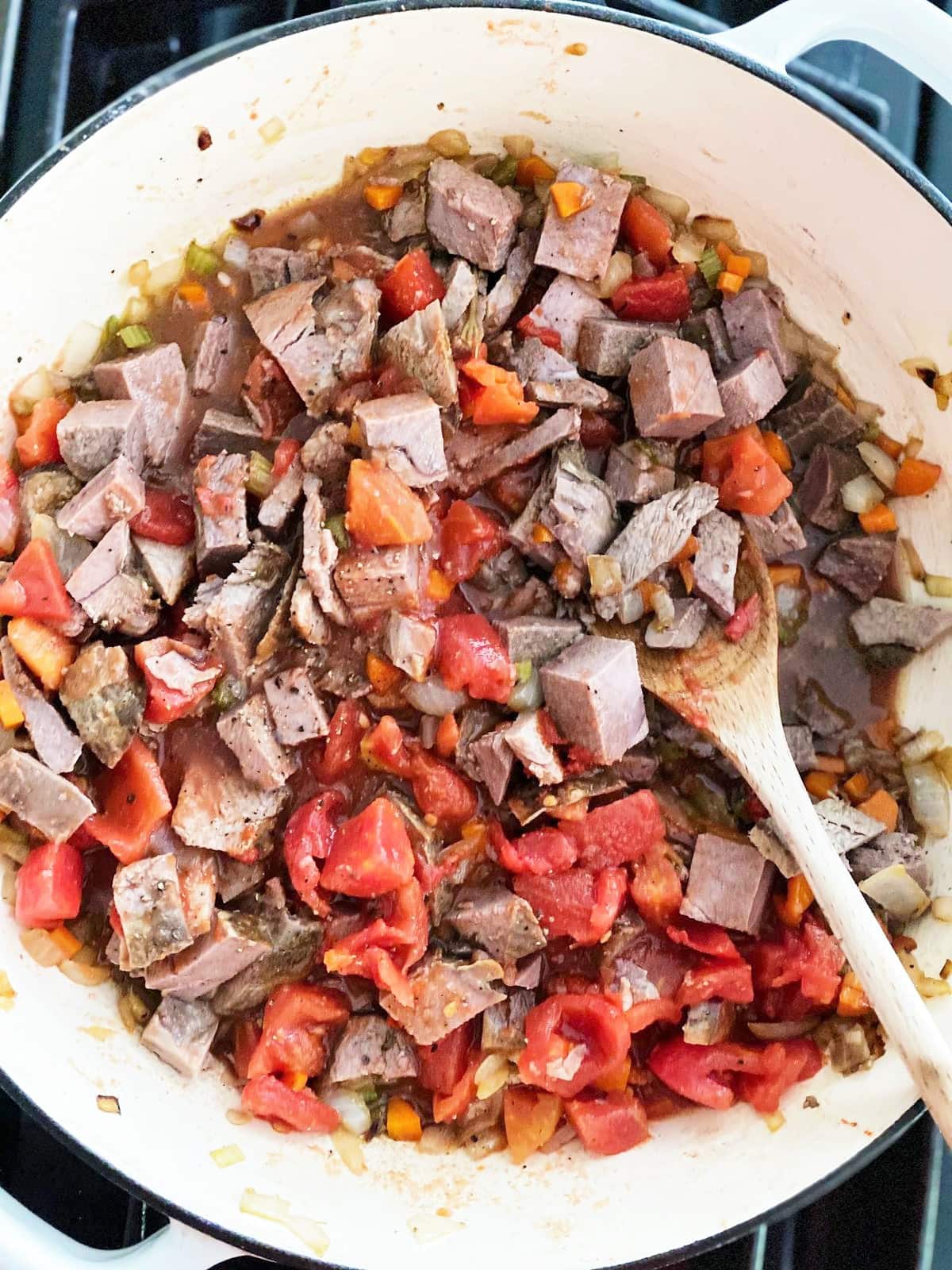 Top down image of large cooking pot with cooked vegetables, diced leftover roast lamb and tinned tomatoes.