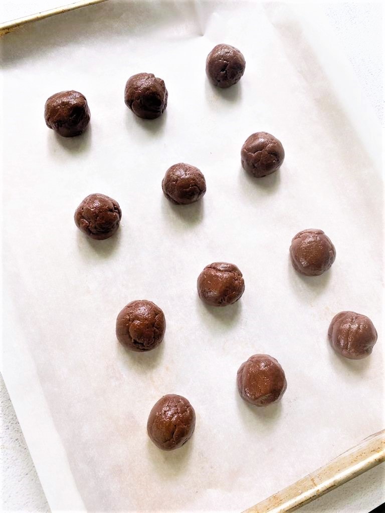 A top down image of a tray lined with baking paper topped with balls of raw chocolate cookie dough.