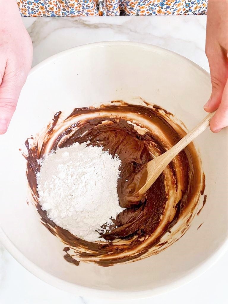 Top down image of mixing bowl containing chocolate spread, flour and a wooden spoon.