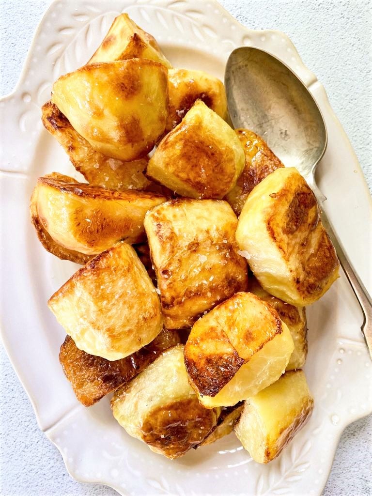 Close up image of white dish filled with crispy roasted potatoes and a serving spoon.