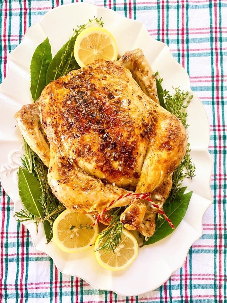 Top down image of whole roast chicken, with lemon, fresh thyme and bay leaves.