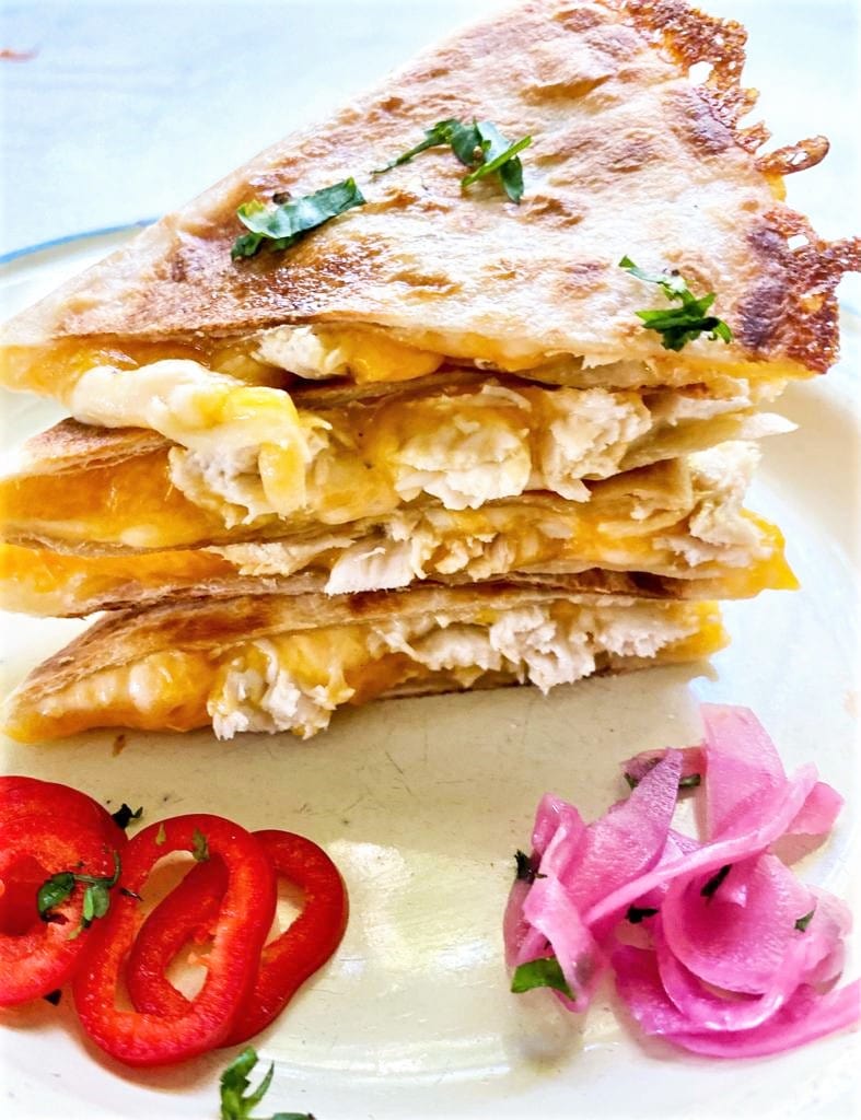 Close up image of a plate of leftover turkey and cheese quesadillas piled high and garnished with red chili and pickled red onions