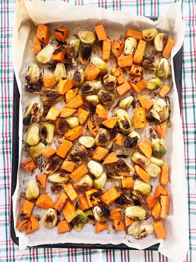 Top down image of baking sheet lined with baking paper containing roasted brussel sprouts and sweet potato 