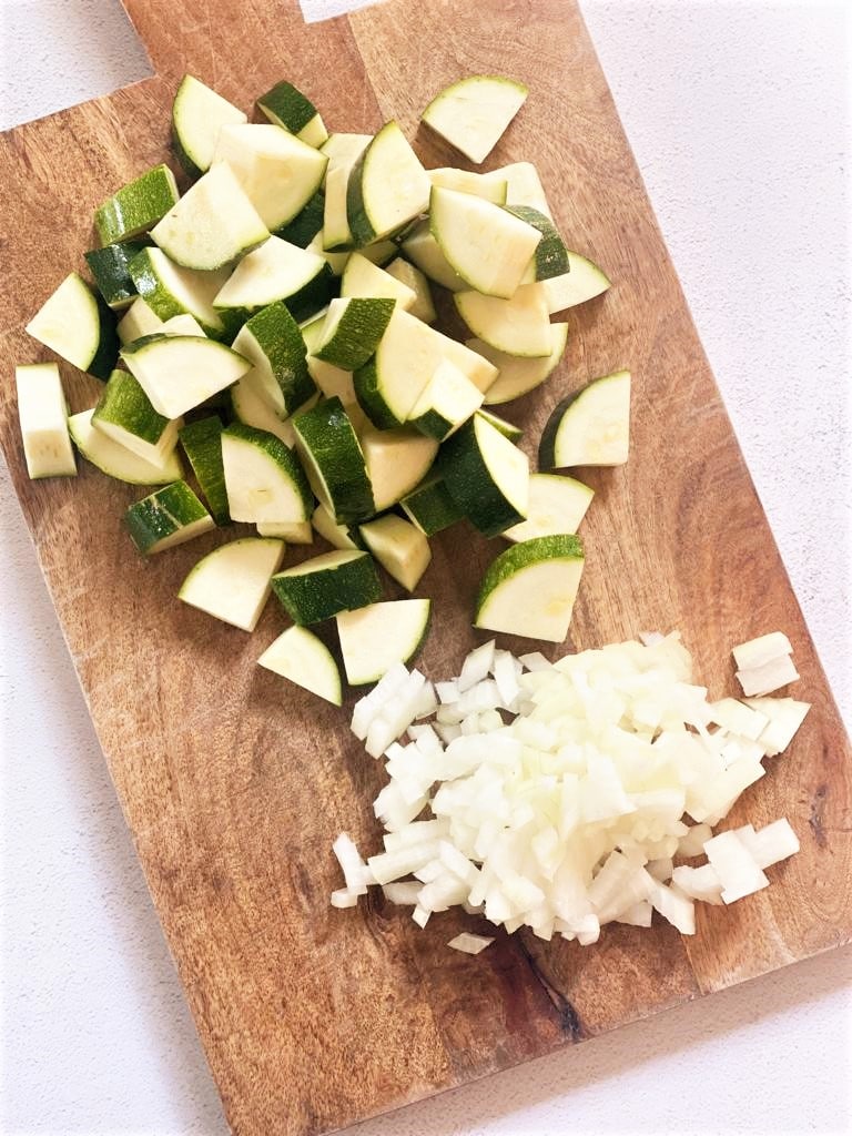 Chopped zucchini and onion on a wooden chopping board.