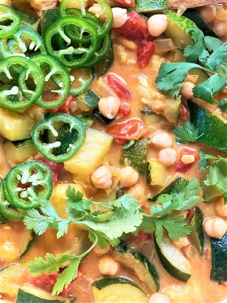 Close up image of cooked zucchini curry topped with a scattering of freshly chopped green chilies and cilantro.