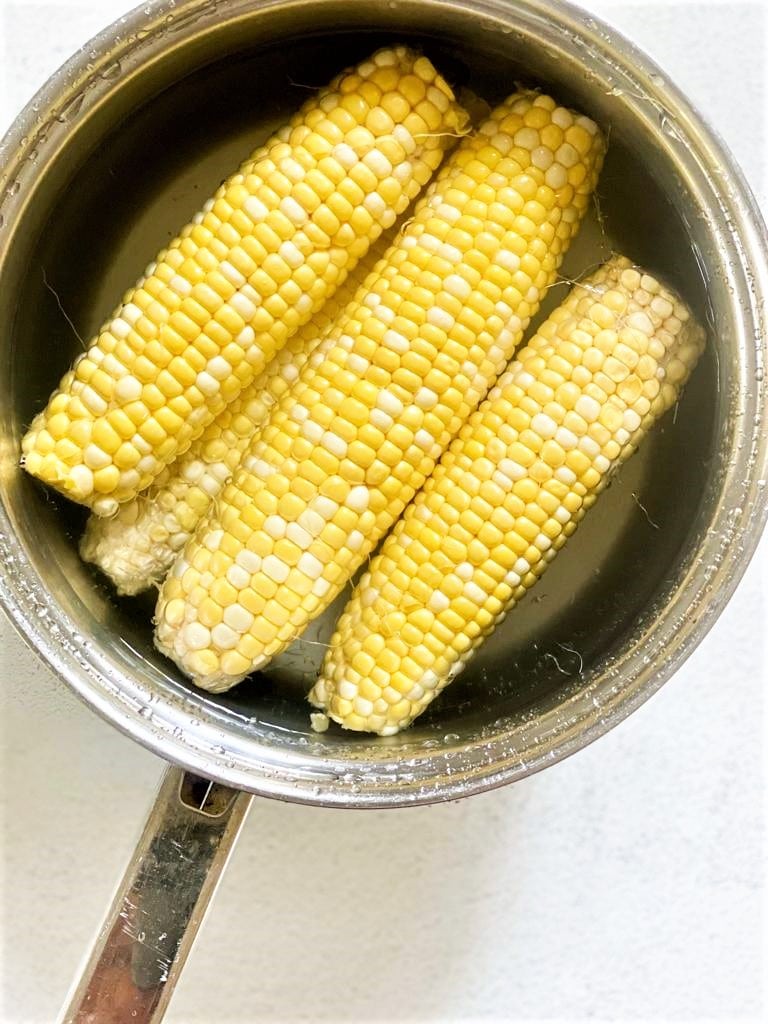 A pan containing 4 ears of corn, covered in water
