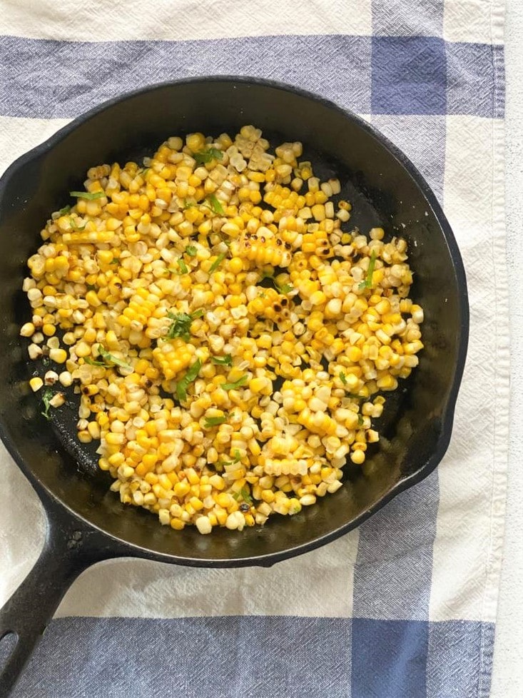 Charred corn kernels in a cast iron skillet with butter and freshly chopped cilantro