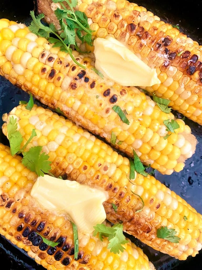 Close up image of charred corn with melted butter and a freshly chopped cilantro