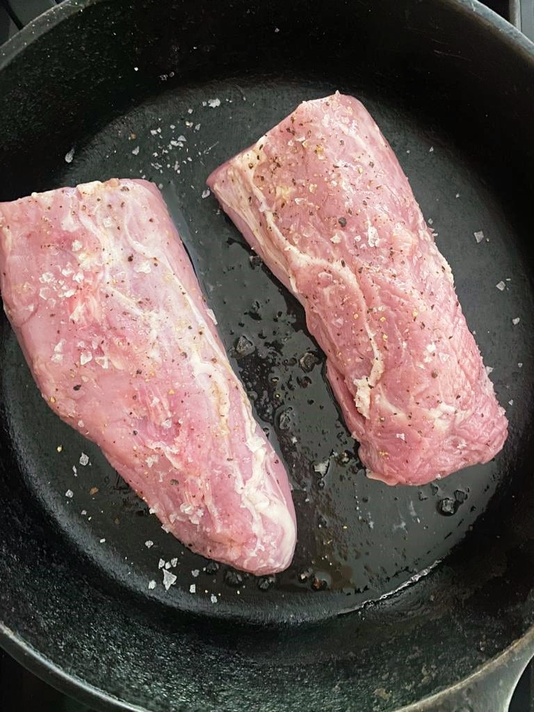 Raw pork tenderloin cut in half and placed into a cast iron skillet