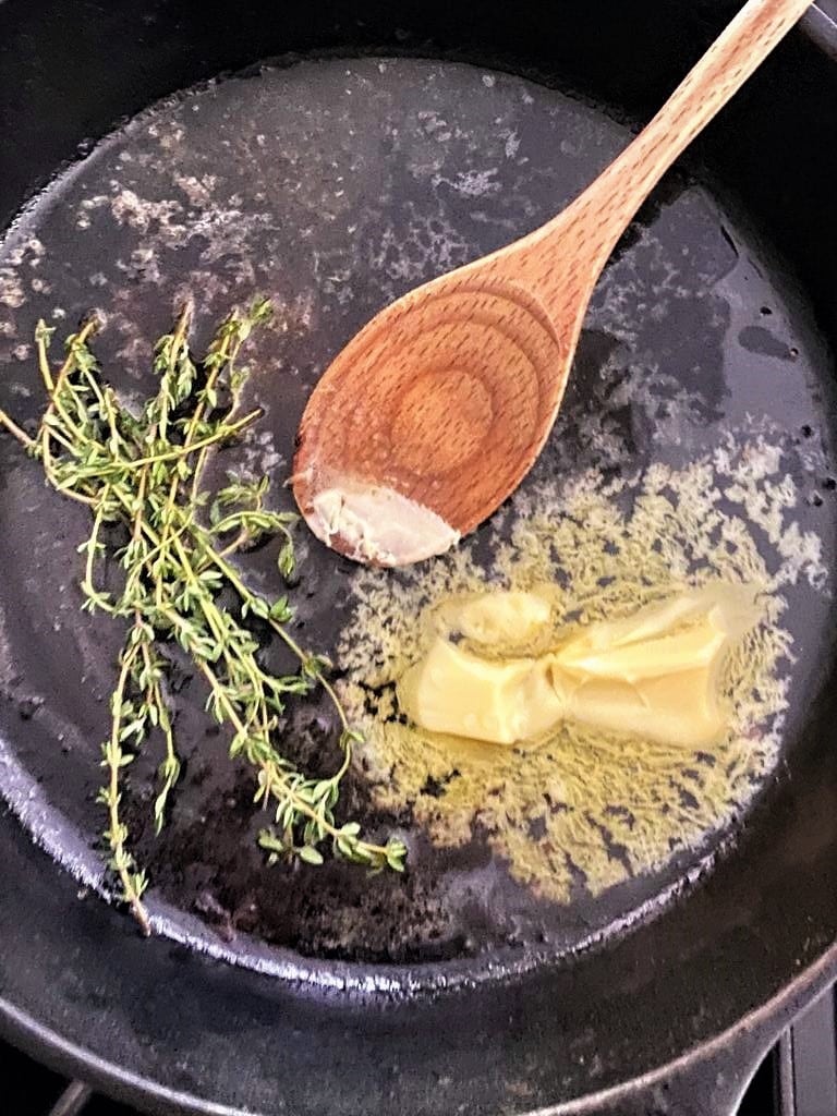 Cast iron skillet with butter, fresh sprigs of thyme and pork cooking juices