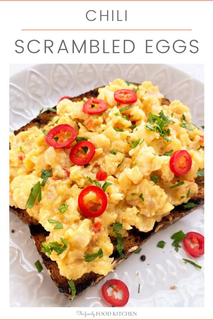 Pinnable image with recipe title and white plate with a slice of toasted granary bread topped with chili scrambled eggs and garnished with slices of red chili and freshly chopped parsley
