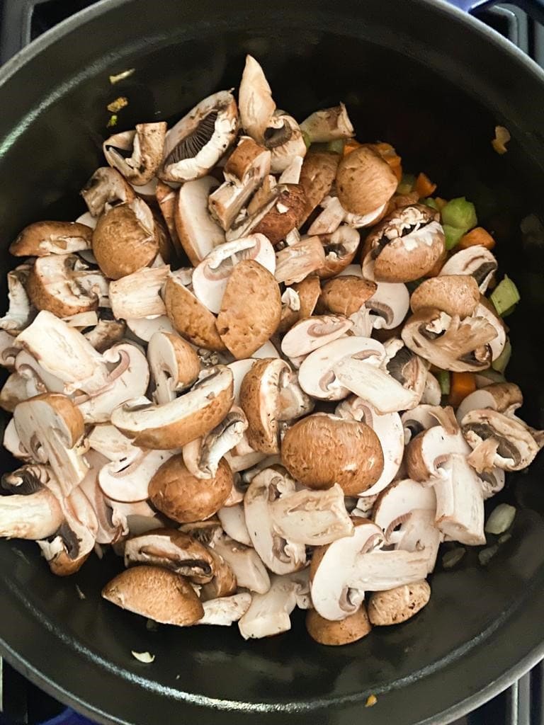 Cast iron pot with cooked vegetables and sliced mushrooms added on top