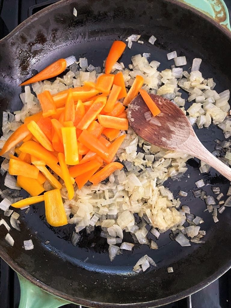 Chopped onions and bell peppers sauteing in a cast iron skillet
