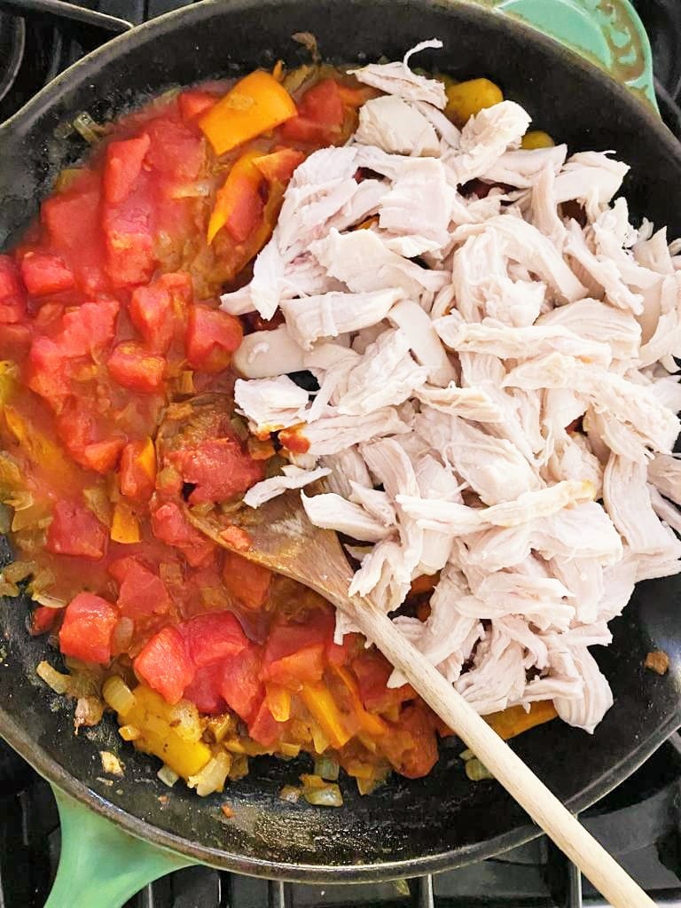 Cast iron skillet with sauteed vegetables and added canned chopped tomatoes and shredded cooked chicken