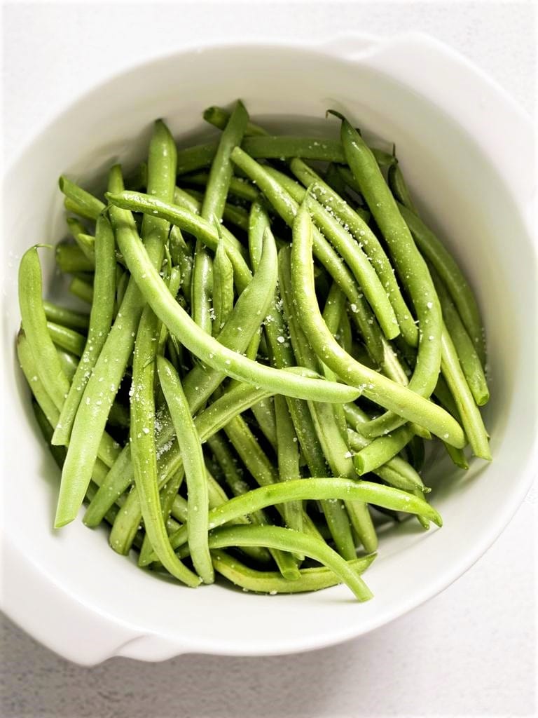 A white bowl with raw green beans sprinkled with sea salt