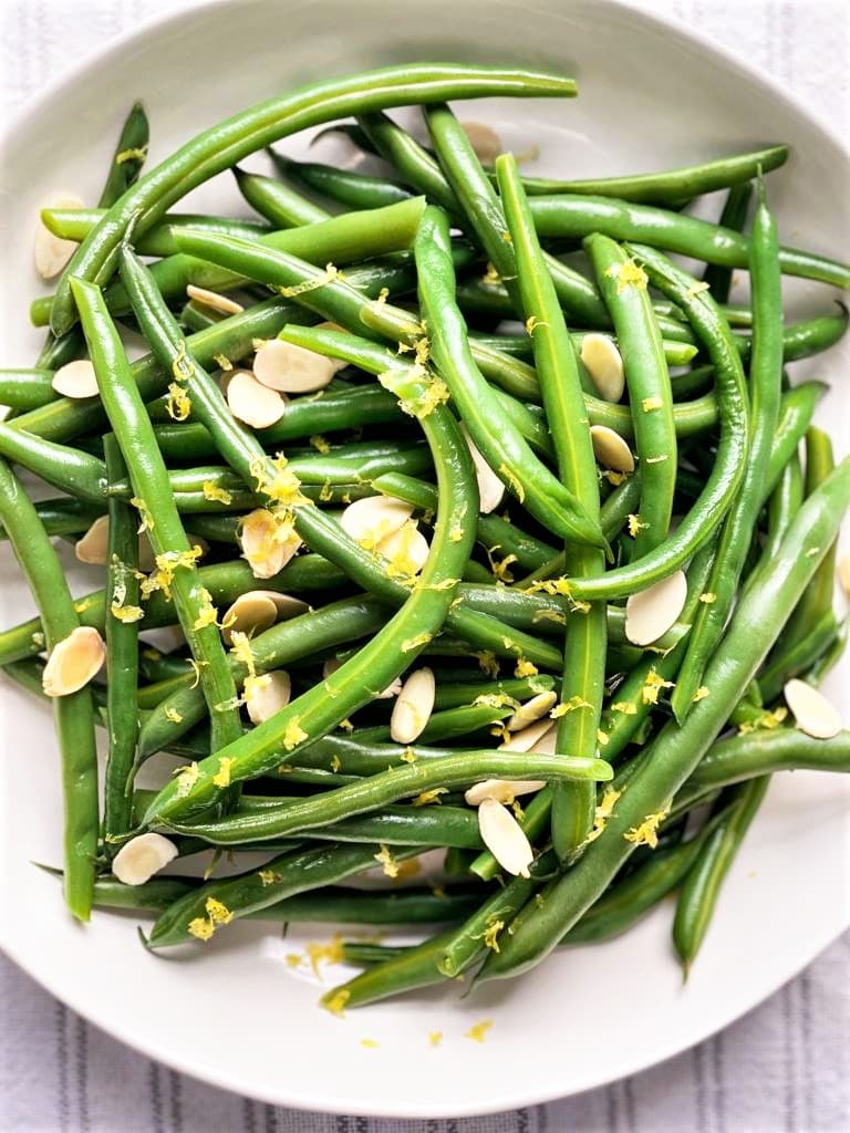 White bowl with cooked green beans, slivered almonds and lemon zest 