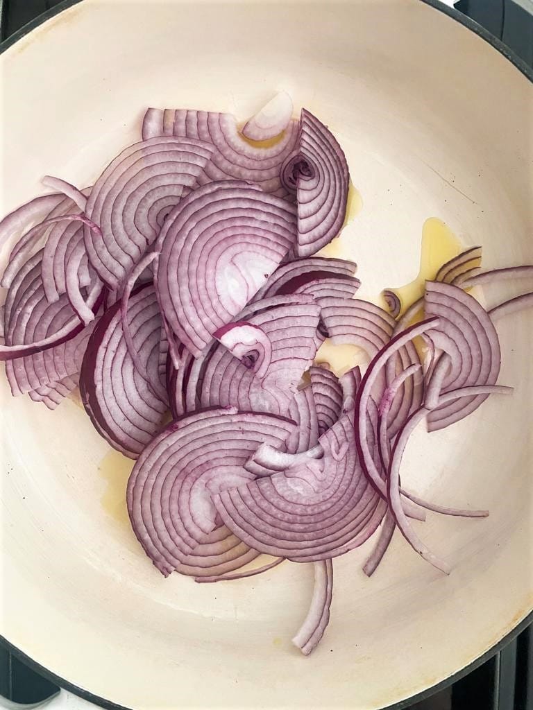 A cast iron pot with olive oil and sliced red onion.