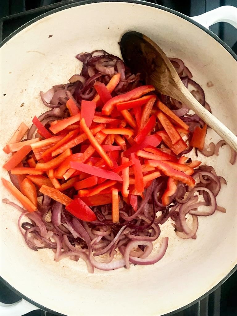 A cast iron pot, with cooked red onion and red bell peppers.