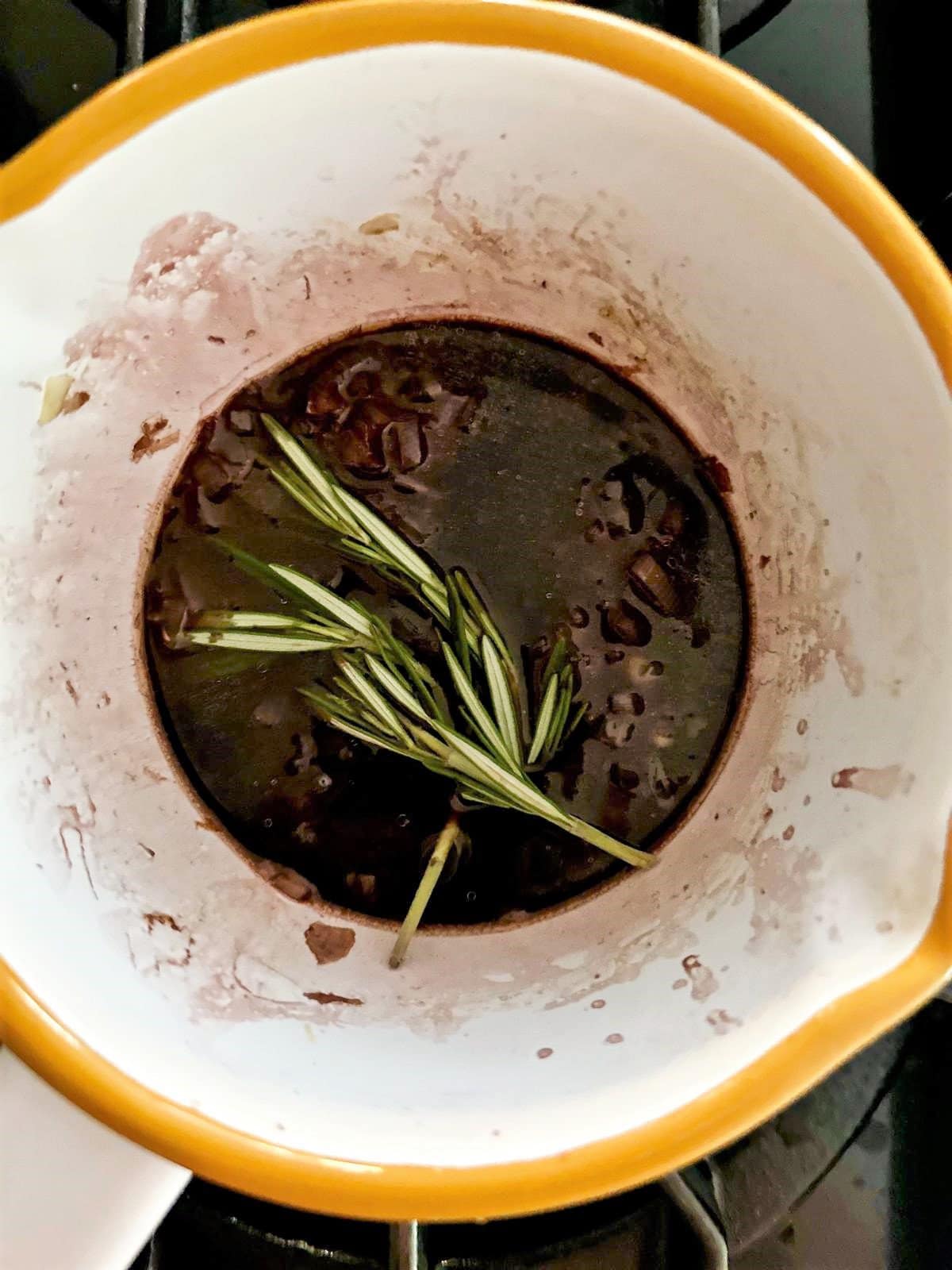 Small saucepan filled with shallots, red wine, broth and sprig of fresh rosemary.