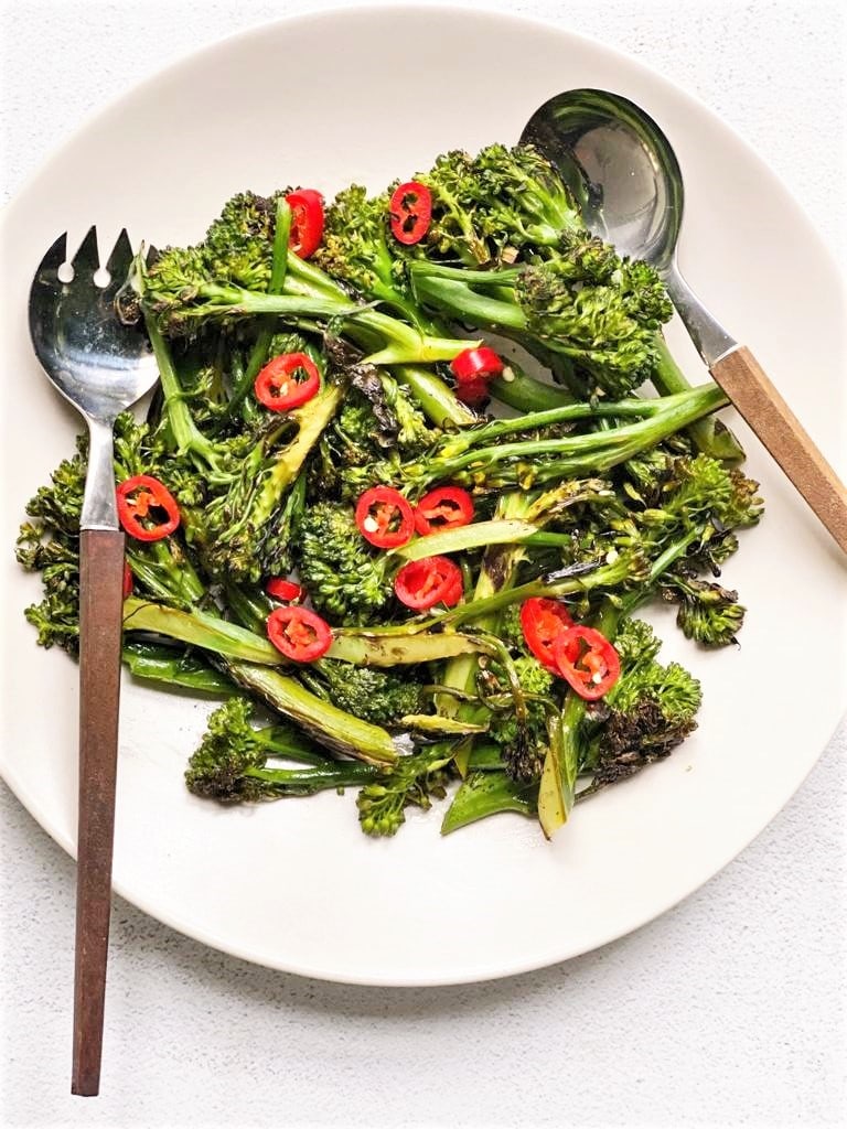 plate of charred broccolini garnished with sliced red chili and serving fork and spoon