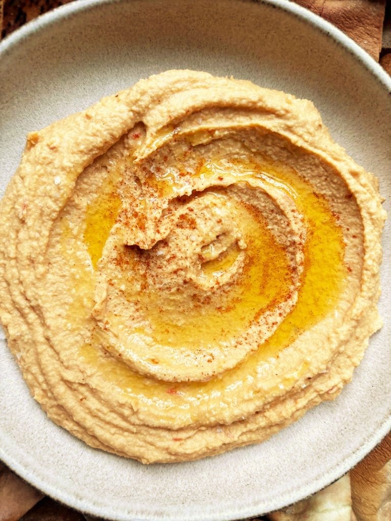 bowl filled with harissa hummus, topped with a drizzle of olive oil and a sprinkle of smoked paprika