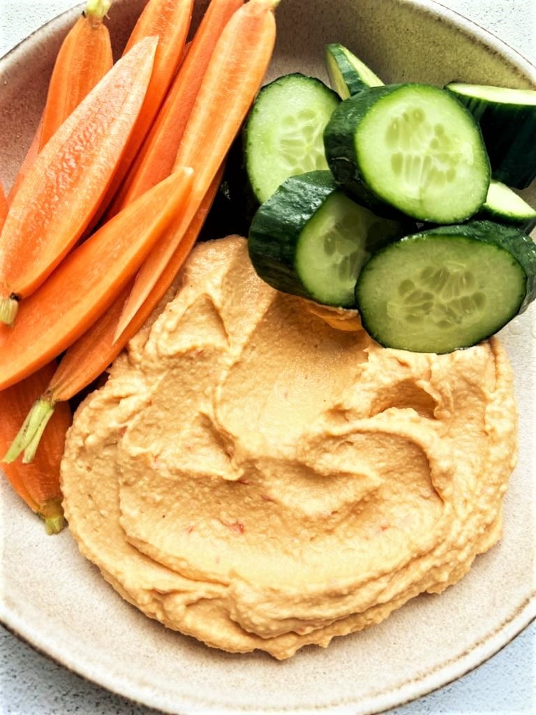 bowl filled with spicy harissa hummus, served with wedges of cucumber and batons of raw carrot