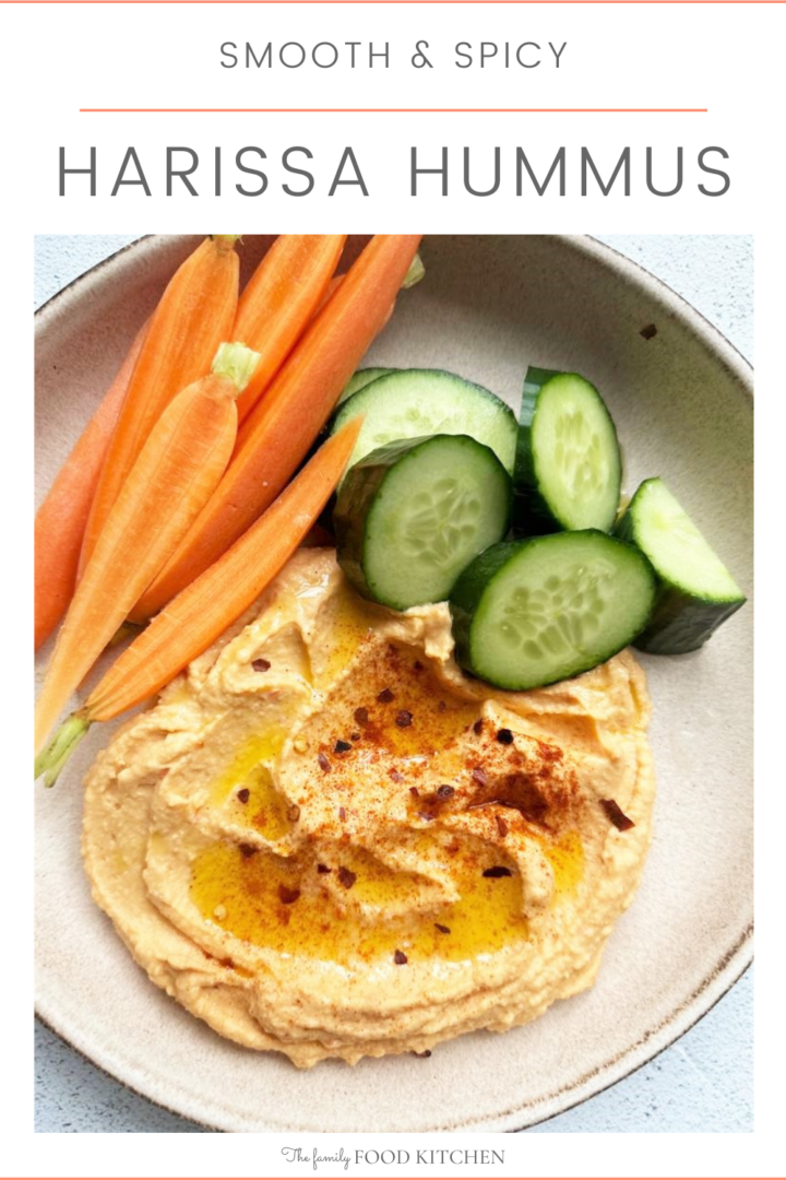 Pinnable image with recipe title and bowl filled with spicy harissa hummus, served with wedges of cucumber and batons of raw carrot