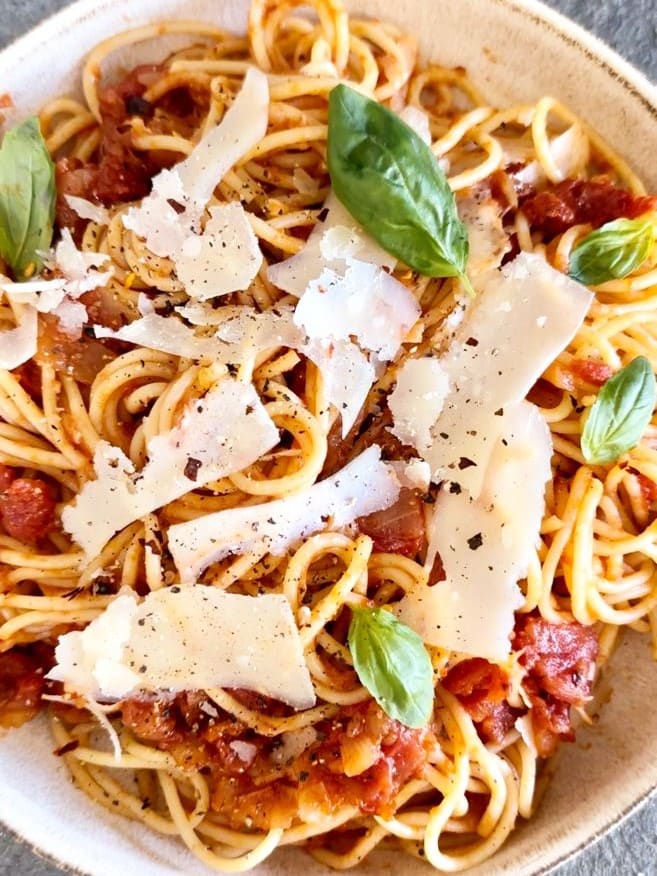 Dutch oven filled with spaghetti arrabiata and garnished with Parmesan cheese and fresh basil