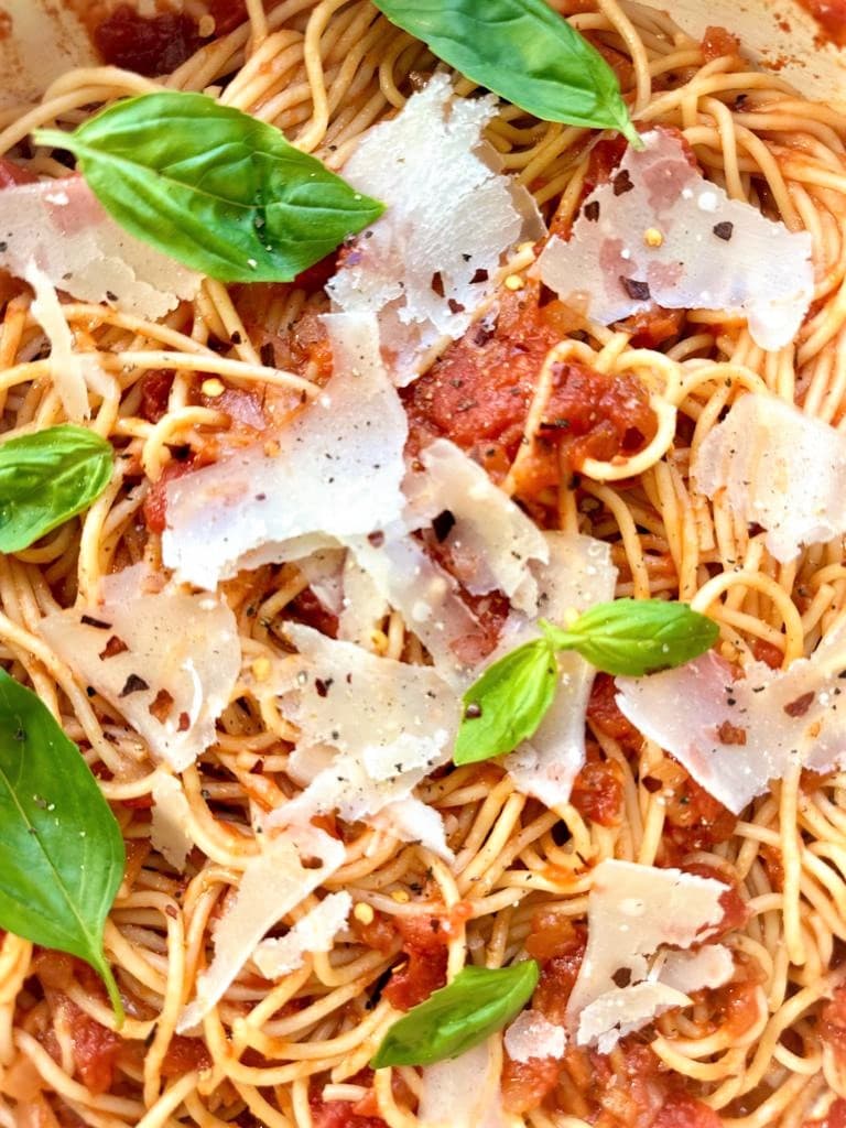 close up image of spaghetti arrabiata and garnished with Parmesan cheese, fresh basil and cracked black pepper