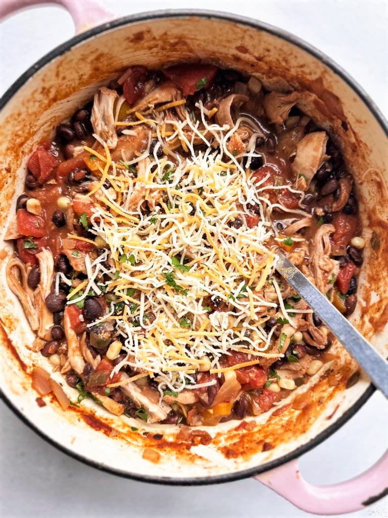 Dutch oven filled with cooked pulled chicken black bean chili topped with shredded cheese and chopped cilantro