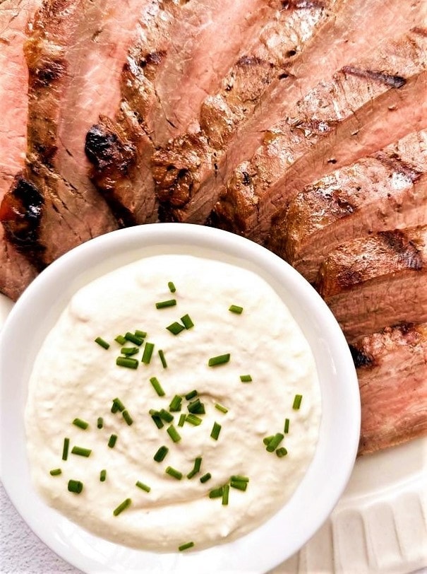 Plate of sliced grilled beef with a bowl of horseradish aioli topped with freshly chopped chives