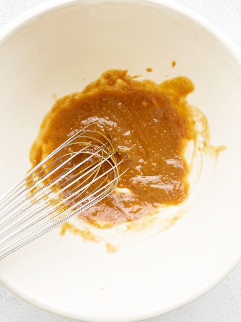 A white bowl filled with the ingredients for a miso glaze being whisked together.