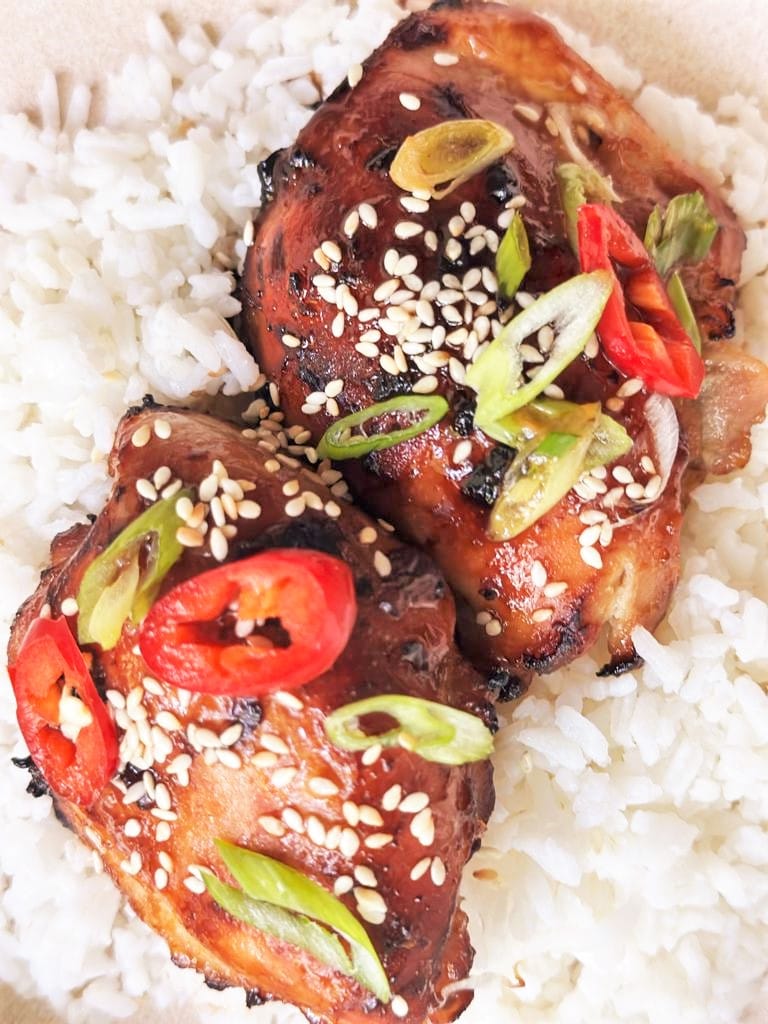 Steamed white rice topped with 2 miso glazed chicken thighs garnished with sesame seeds, sliced green onion and red chili.