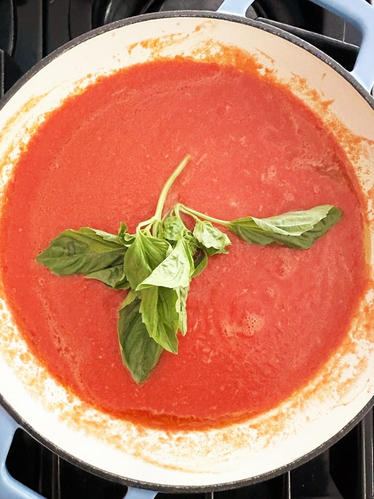 Dutch oven filled with crushed tomato sauce and topped with a sprig of fresh basil.