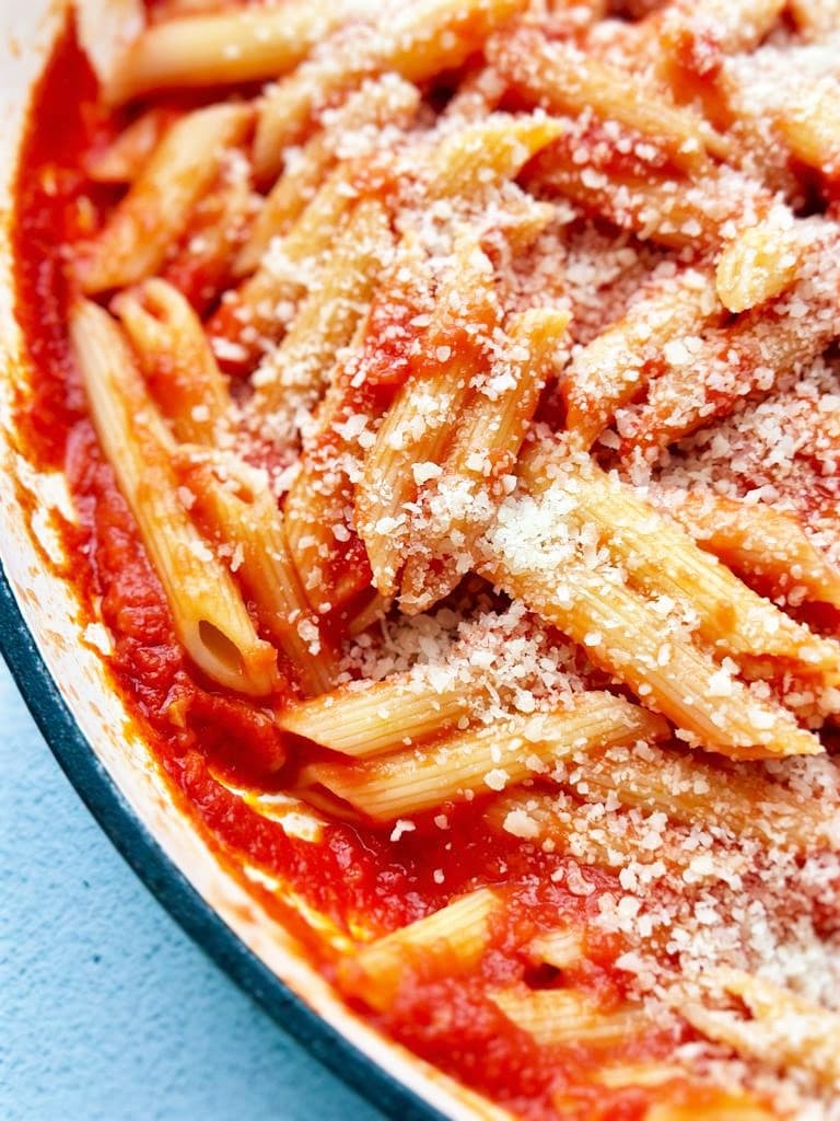 Close up photo of penne pasta in a tomato sauce with a garnish of grated Parmesan cheese.