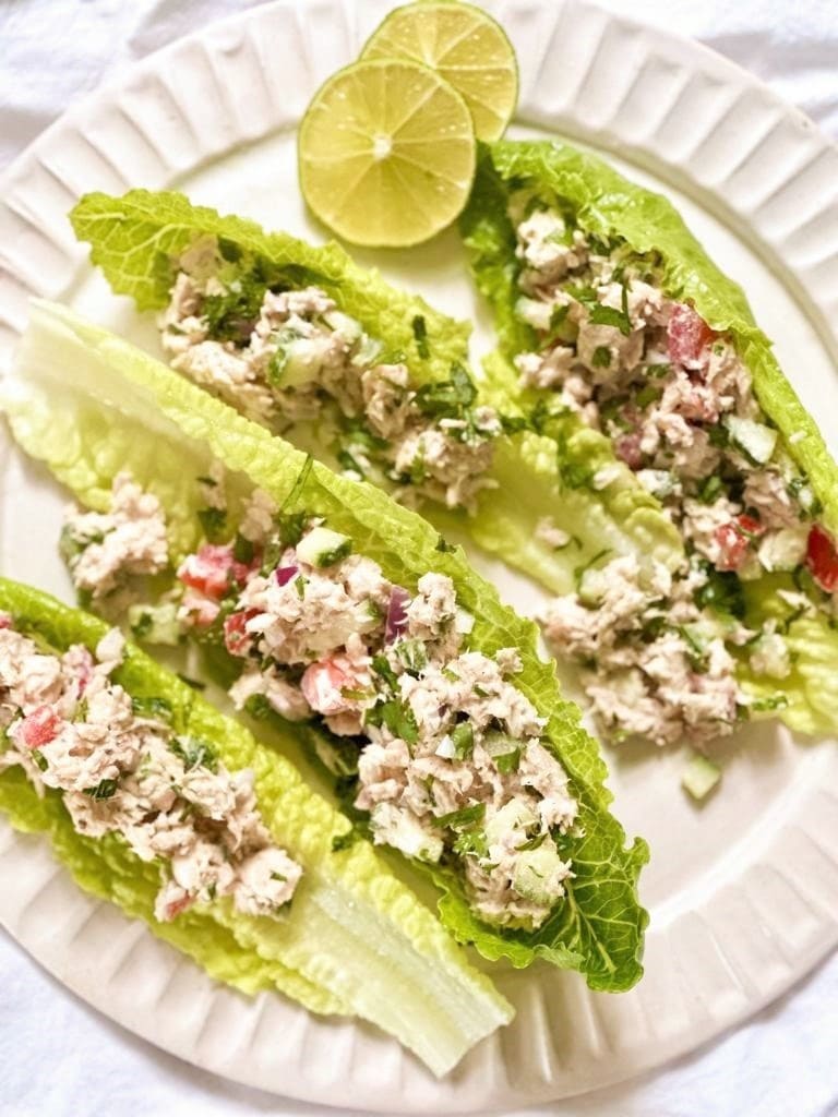 A white plate topped with Mexican tuna salad served in individual salad leaves with a wedge of lime set alongside.