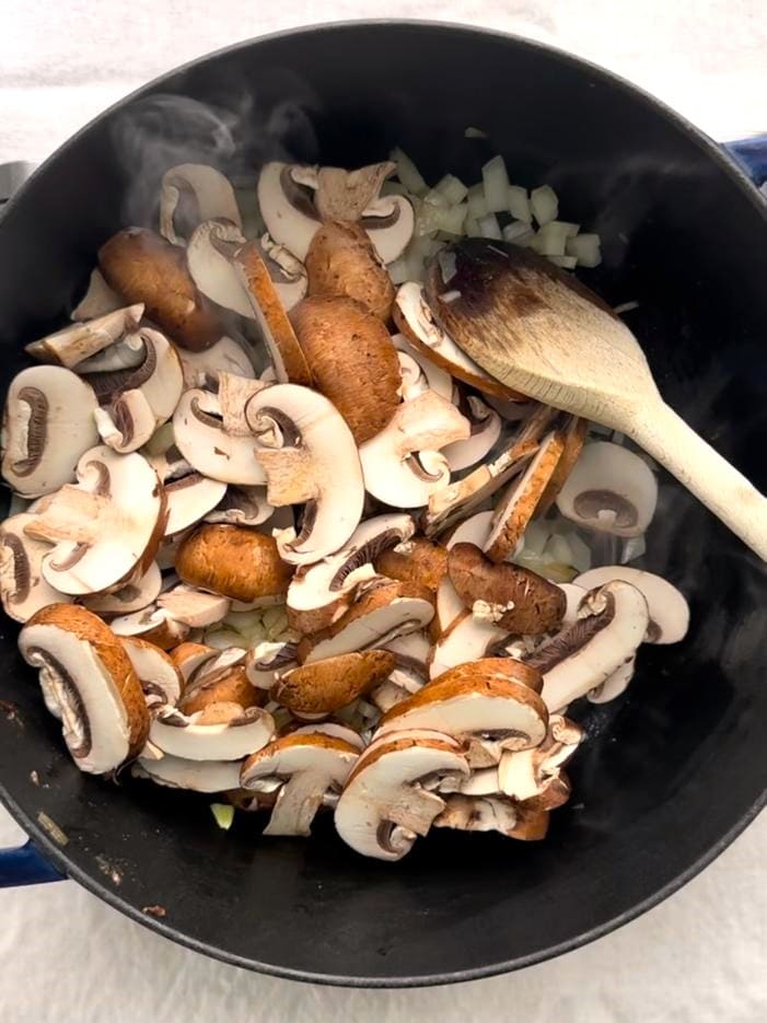 A Dutch oven with sauteed onions and added sliced mushrooms.