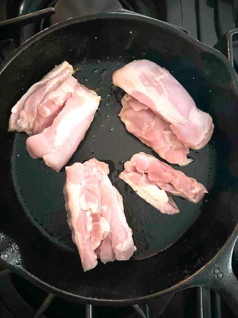 Chicken thighs cooking in a large skillet.
