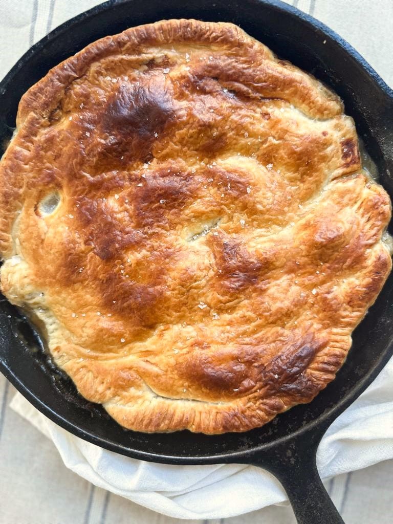 A skillet with chicken pot pie, topped with golden puff pastry.