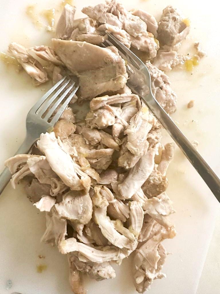 Chicken thighs being shredded on a cutting board using 2 forks.