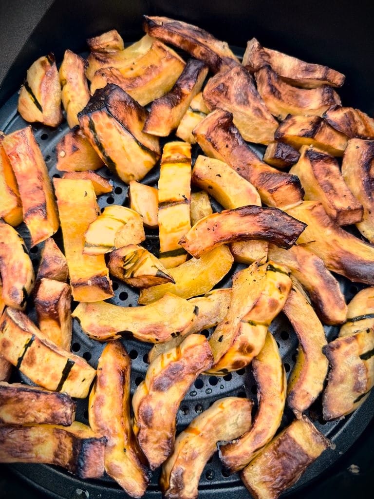 Slices of roasted delicata squash in the air fryer basket.