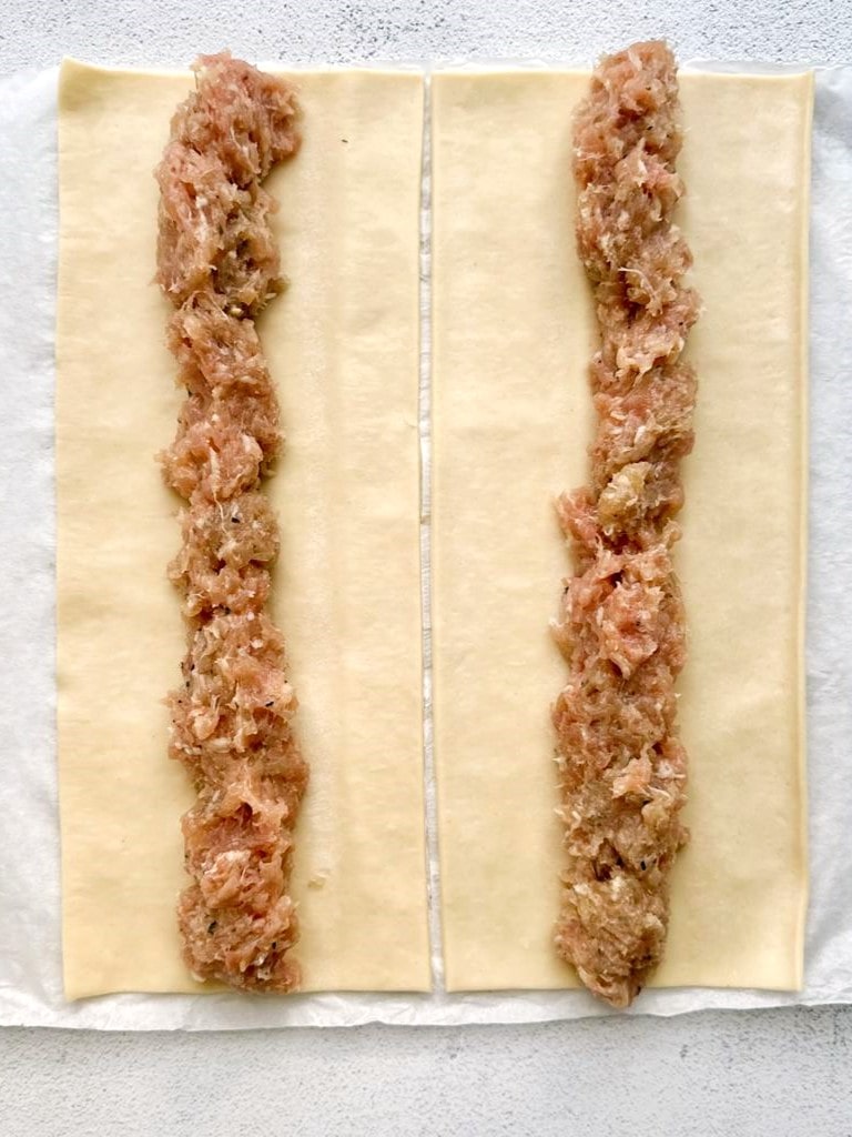 Two strips of puff pastry with a line of chicken sausage mixture down the center of each sheet.