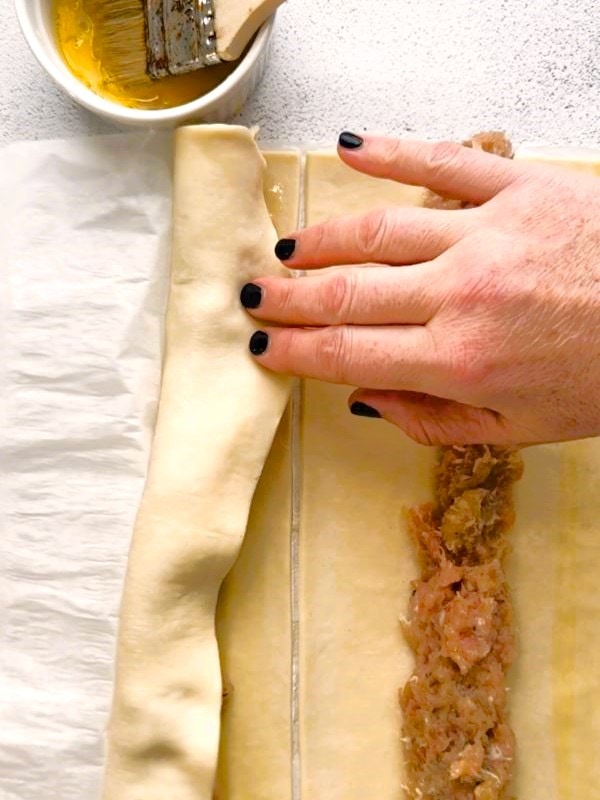 A sheet of puff pastry being rolled over the top of the chicken sausage meat filling.