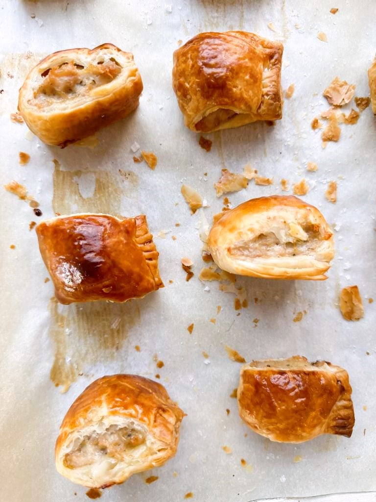 Six chicken sausage rolls set out on a sheet of baking parchment.